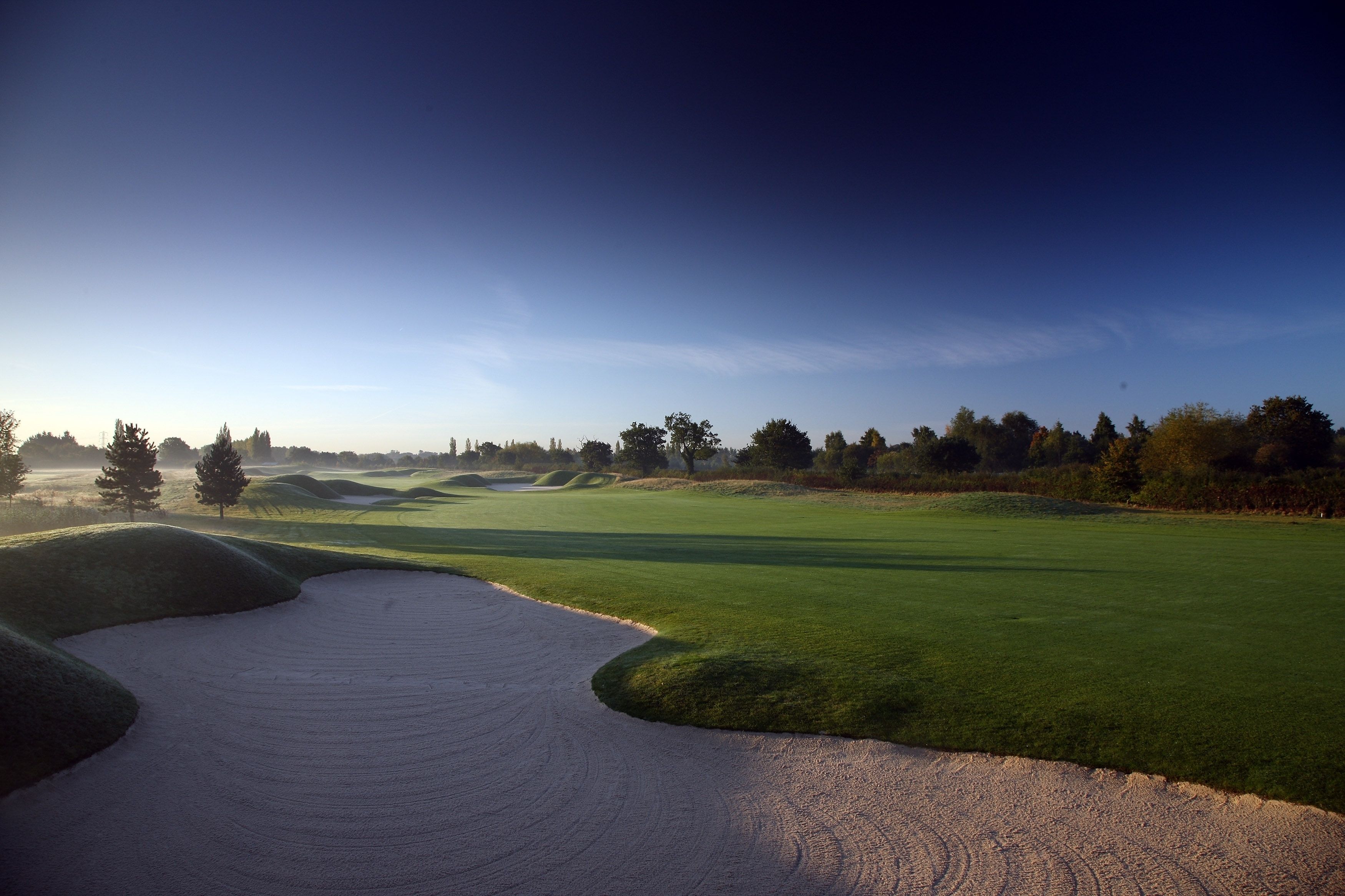 A golf course with sand bunkers, a well-maintained green, and a clear sky.