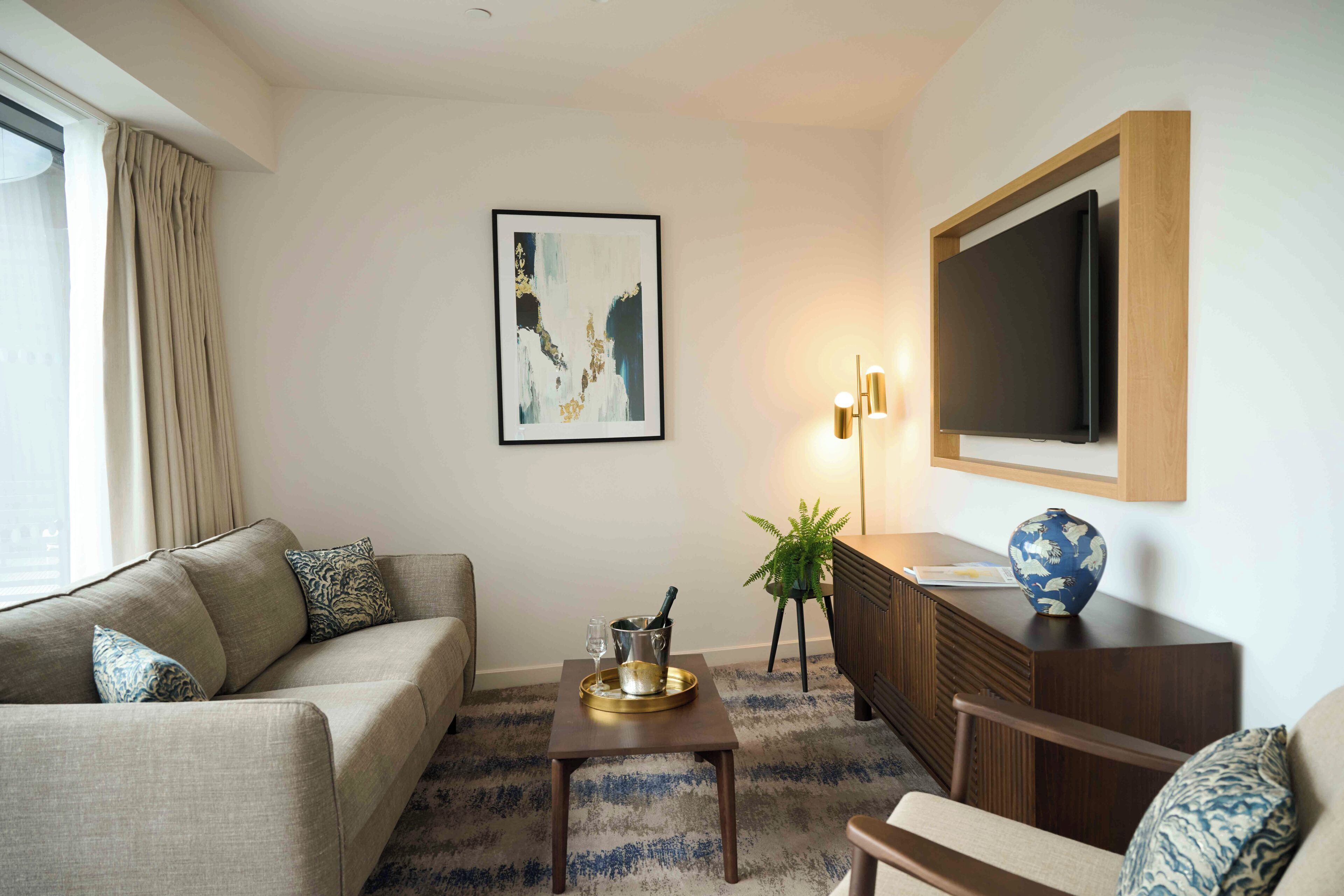 A living room with a sofa, a coffee table with a tray, a TV, a plant, and a painting on the wall.