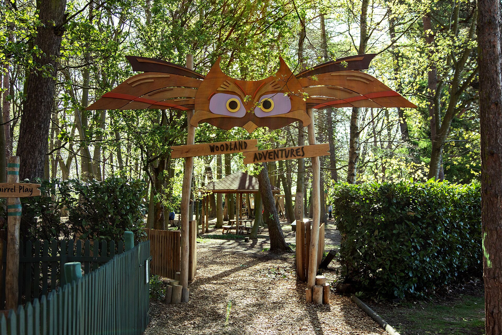 Un letrero de madera con un diseño de cara de gato y la inscripción 'Woodland Adventures', que indica un área o atracción temática.
