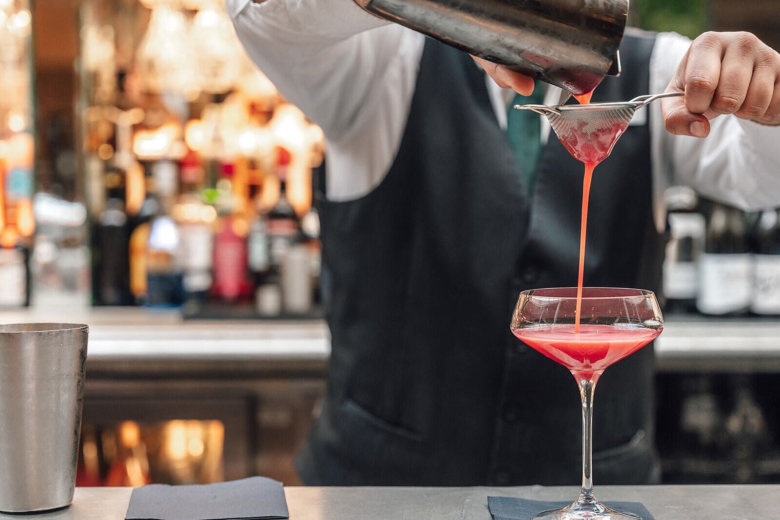 A bartender pouring a drink into a martini glass.