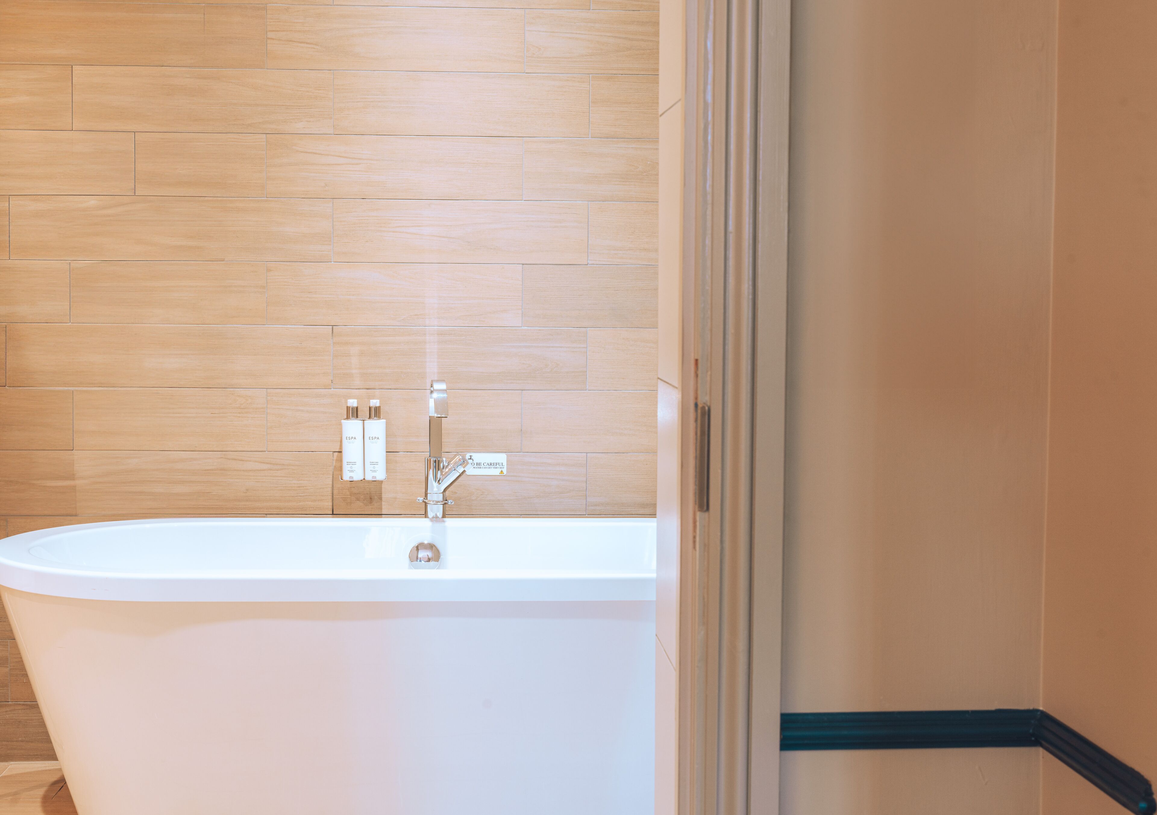 A modern bathroom with a freestanding bathtub, wooden wall tiles, and a visible shower area.