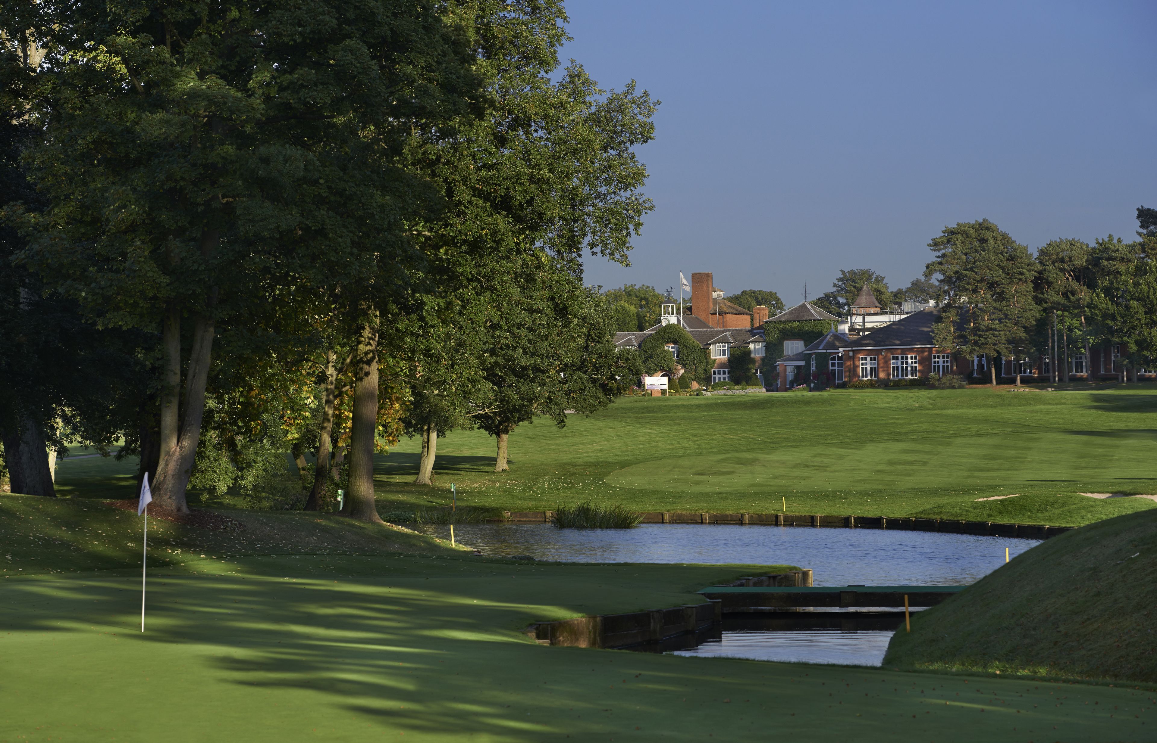 A golf course with a pond, trees, and a building in the background.