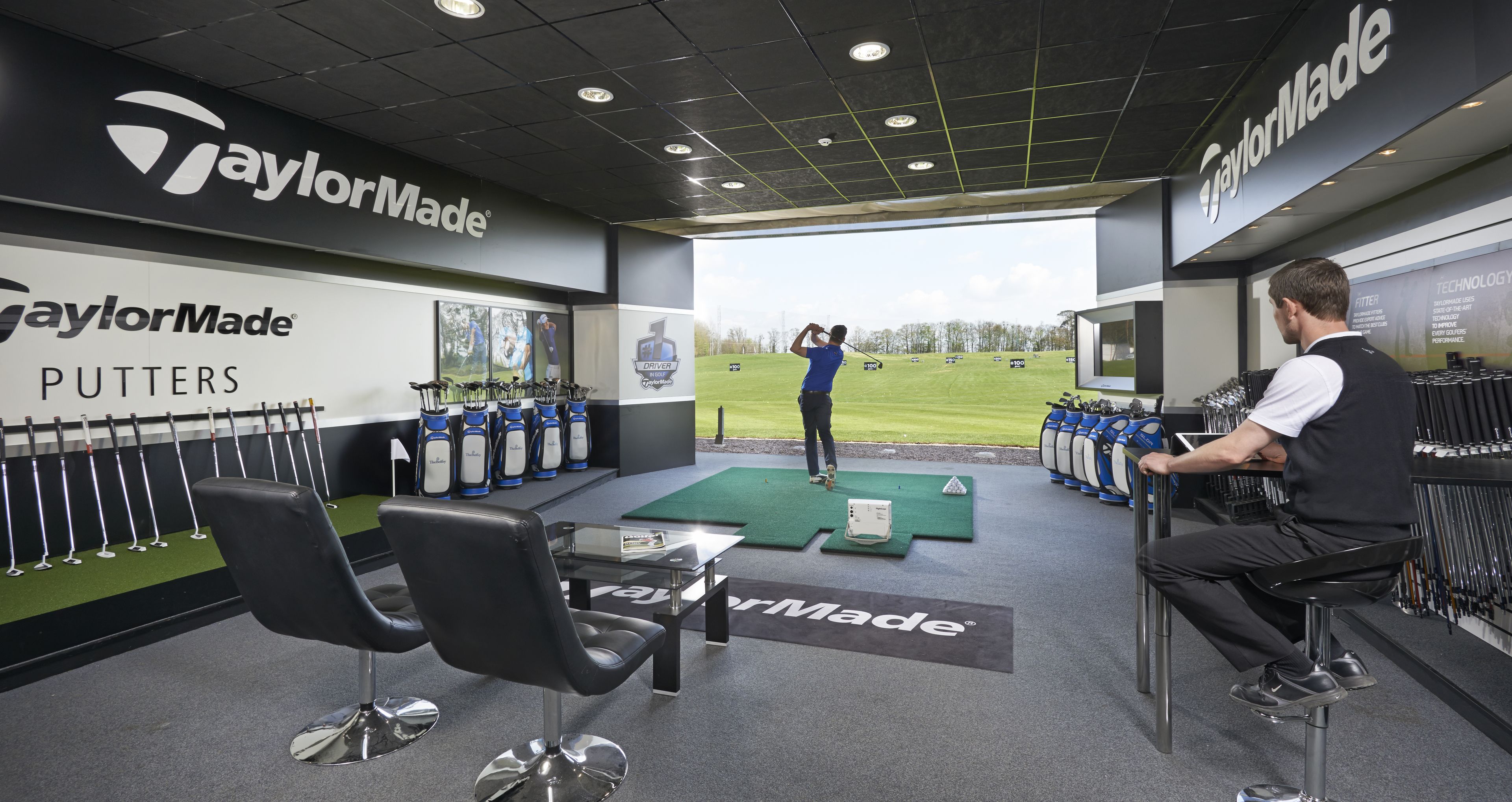 A golf driving range with TaylorMade branded equipment and a putting area.