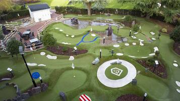 A miniature golf course with a white clubhouse, various holes, and surrounding landscaping.