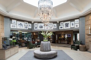 A spacious lobby with a central seating area, a reception desk, framed photographs on the walls, and a chandelier. - The Belfry (Sutton Coldfield)