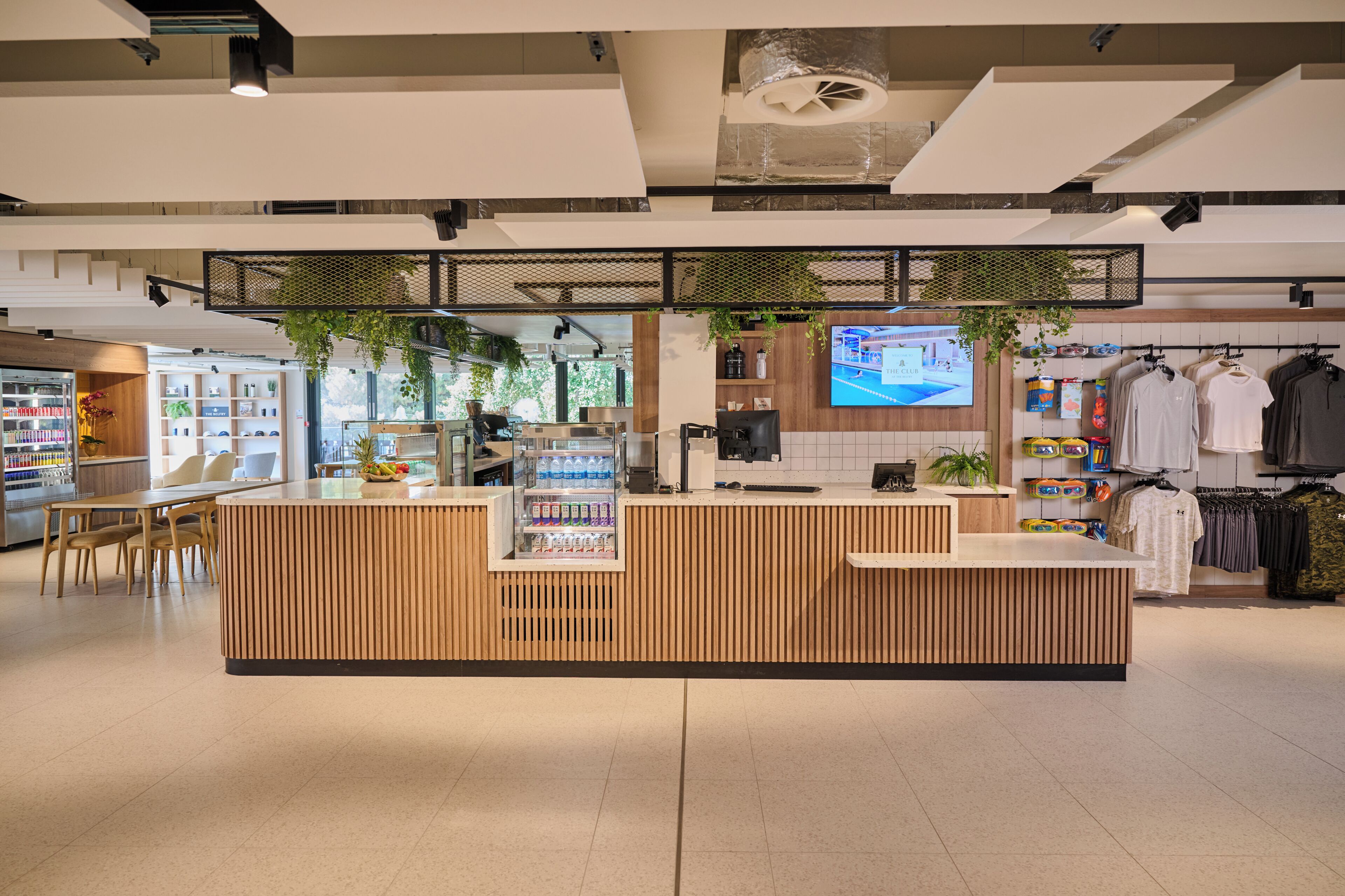 Un espacio comercial moderno con un mostrador de recepción de madera, una zona de estar y percheros para ropa.