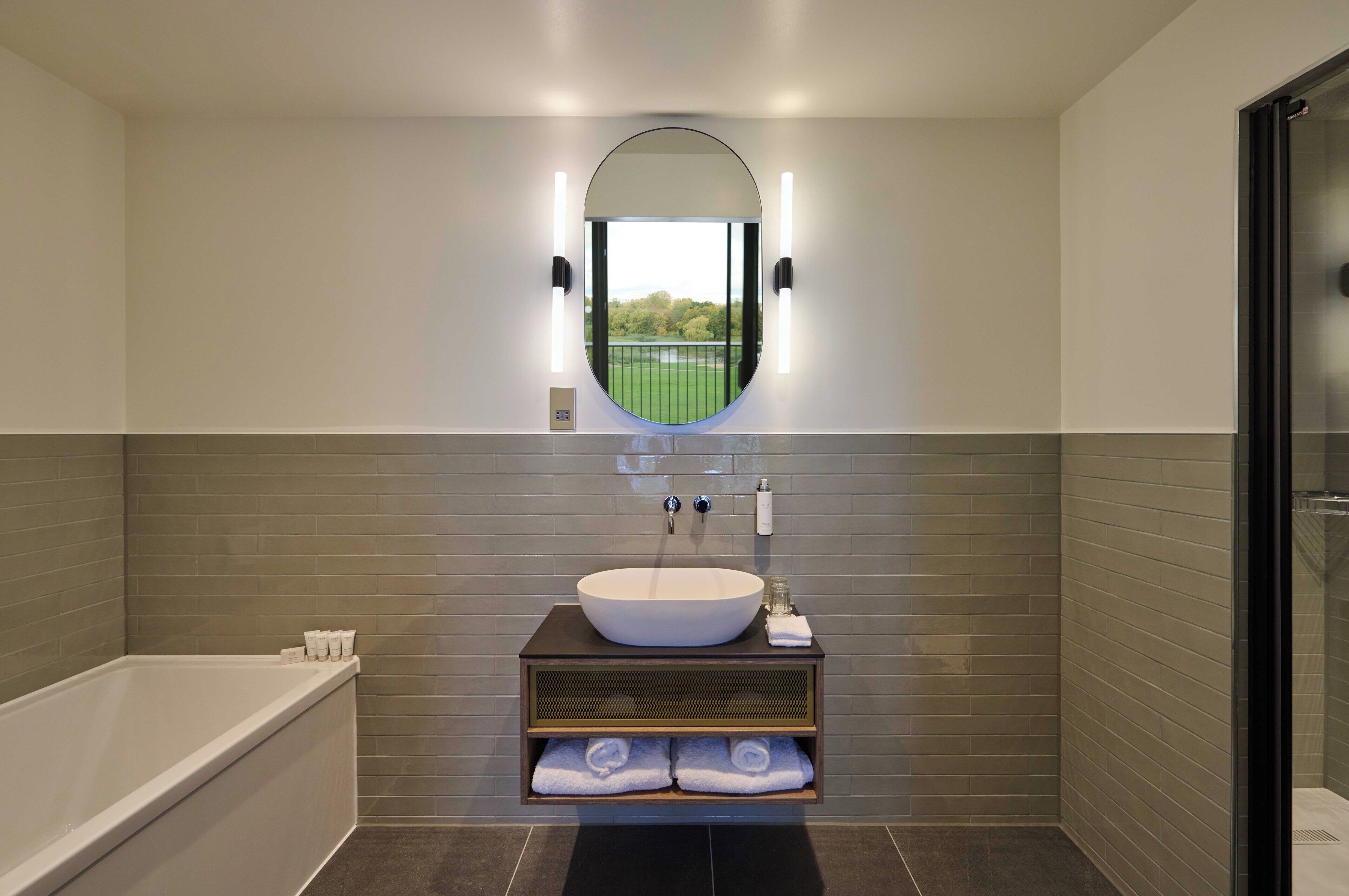 A modern bathroom with a large bathtub, a round mirror, and a built-in sink.