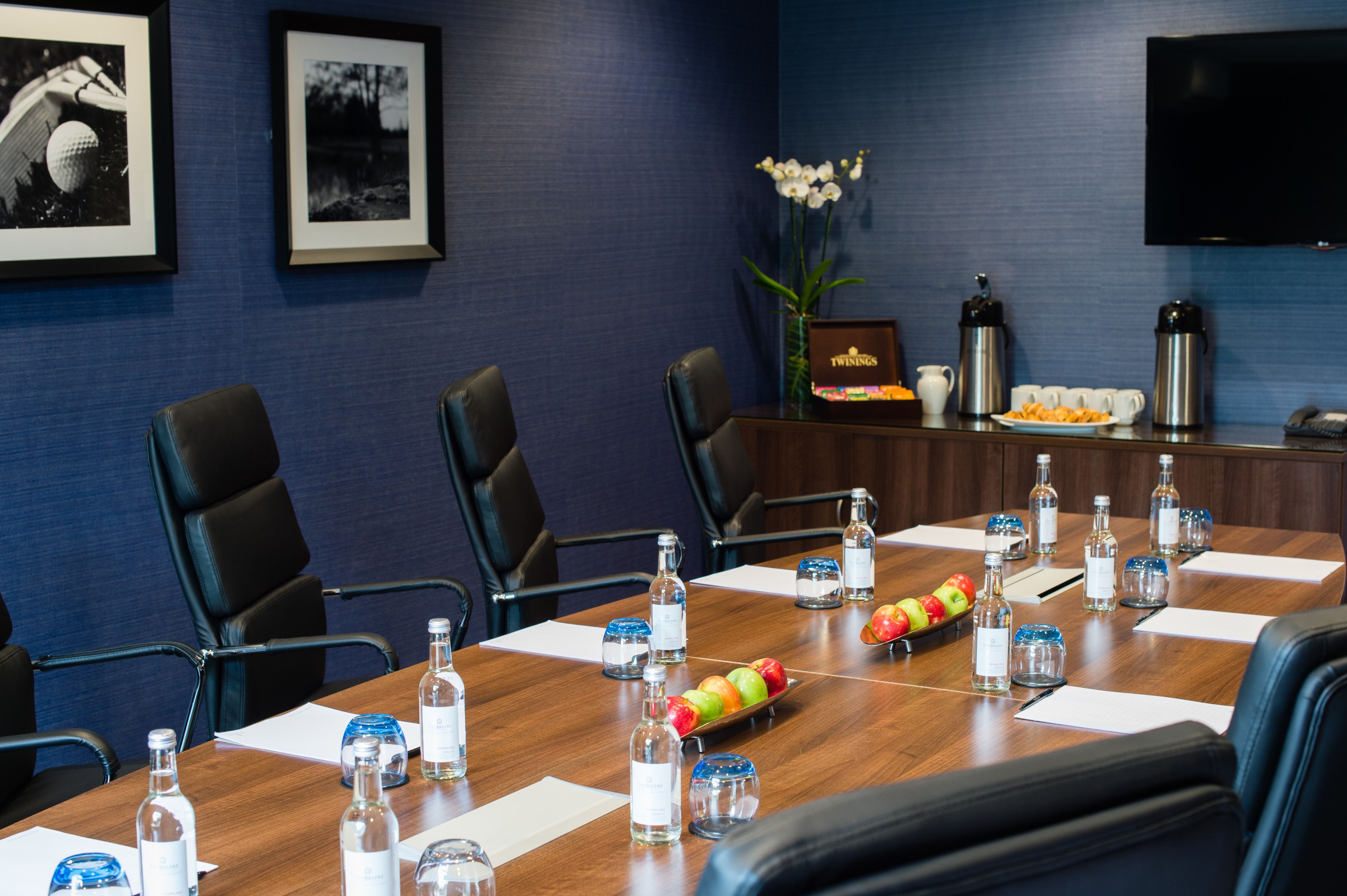 A conference room with a wooden table, chairs, water bottles, a fruit tray, and framed pictures on the wall.