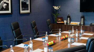A conference room with a wooden table, chairs, water bottles, a fruit tray, and framed pictures on the wall.