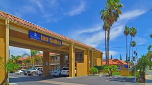 A hotel with a sign reading "Inn Suites" and a red-tiled roof. There are palm trees and a clear blue sky in the background. - Riverside Inn & Suites (Riverside)