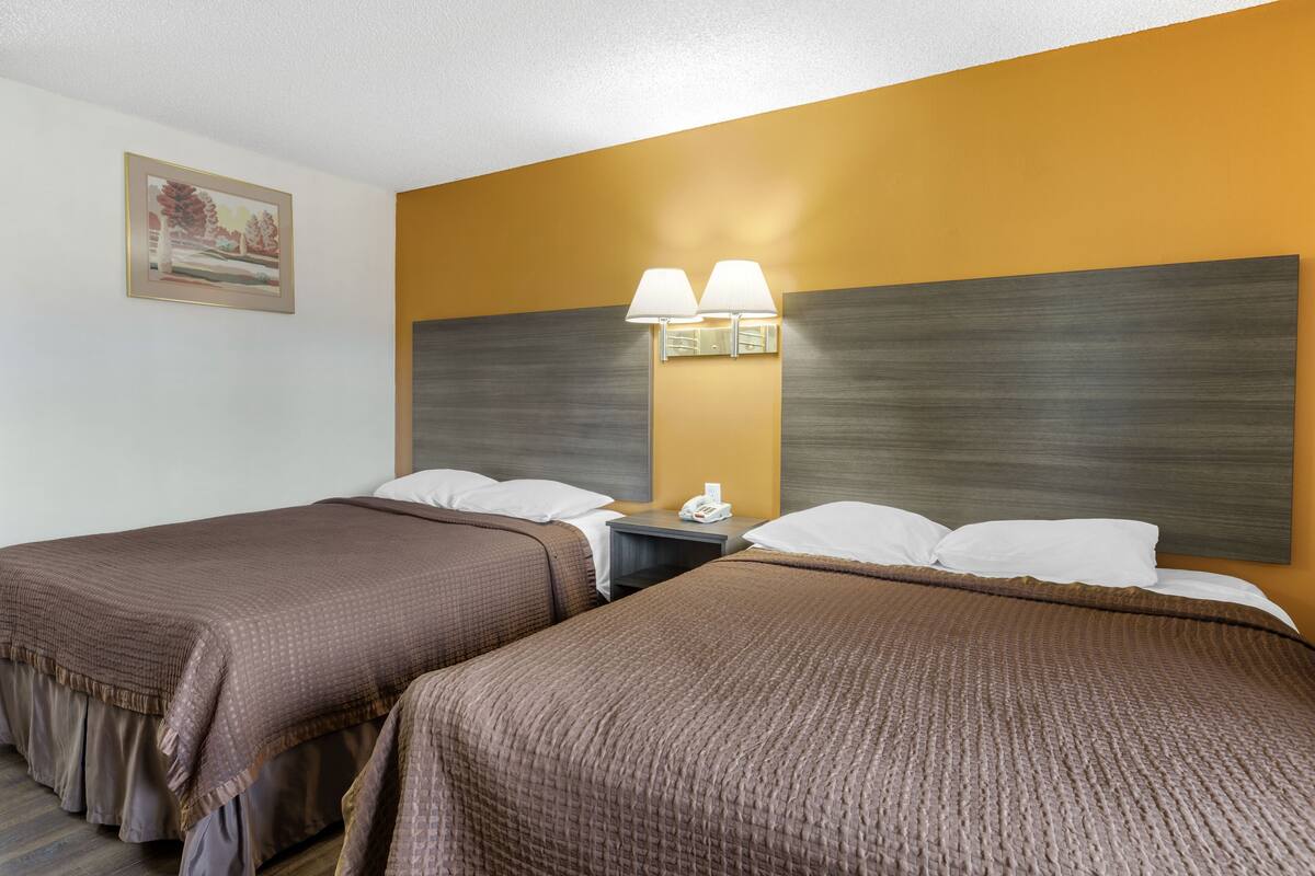 Ett hotellrum med två sängar, ett nattduksbord och en väggmonterad lampa.