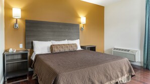 A hotel room with a large bed, two bedside tables, a wall-mounted heater, and two wall-mounted lamps. - Riverside Inn & Suites (Riverside)