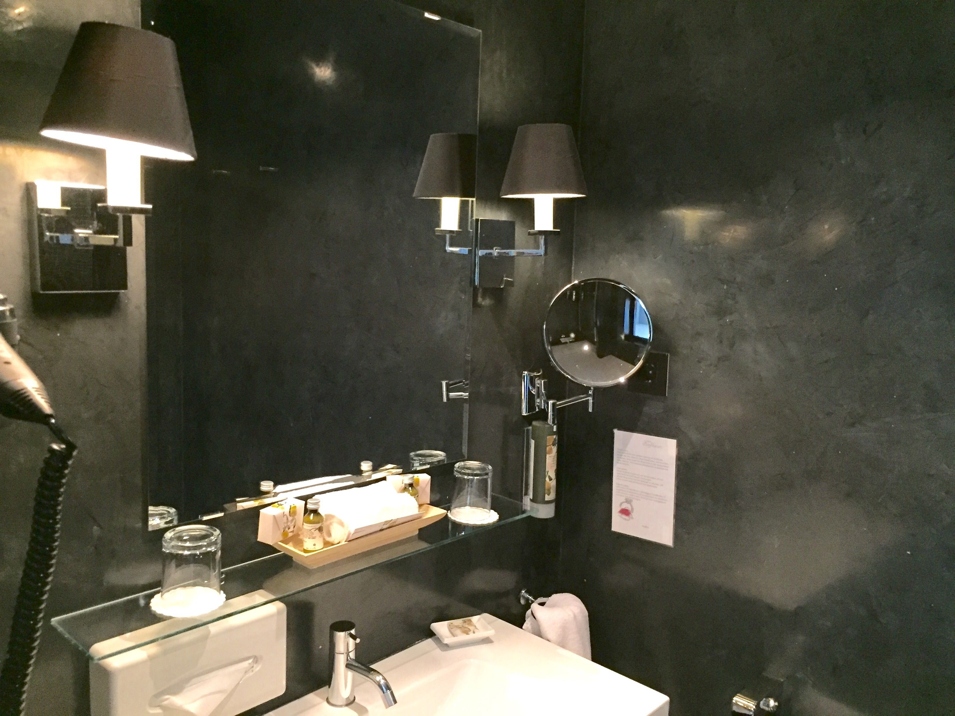 A modern bathroom with a black wall, a white sink, a mirror, and two wall-mounted lamps.