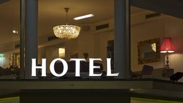 A hotel entrance with a neon sign, a chandelier, and a reception desk.
