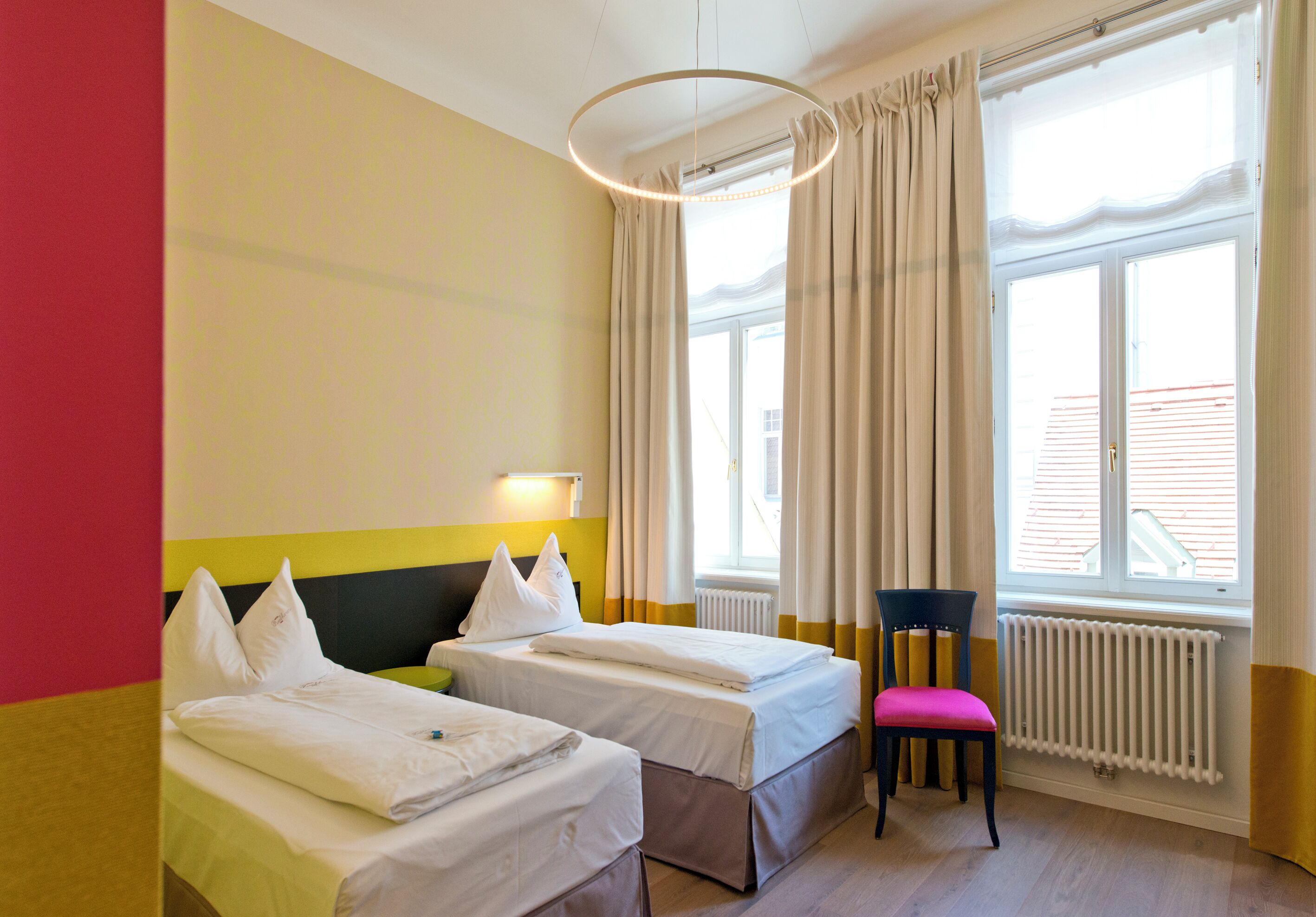 Una habitación de hotel con dos camas, una ventana con cortinas, una silla y un radiador.