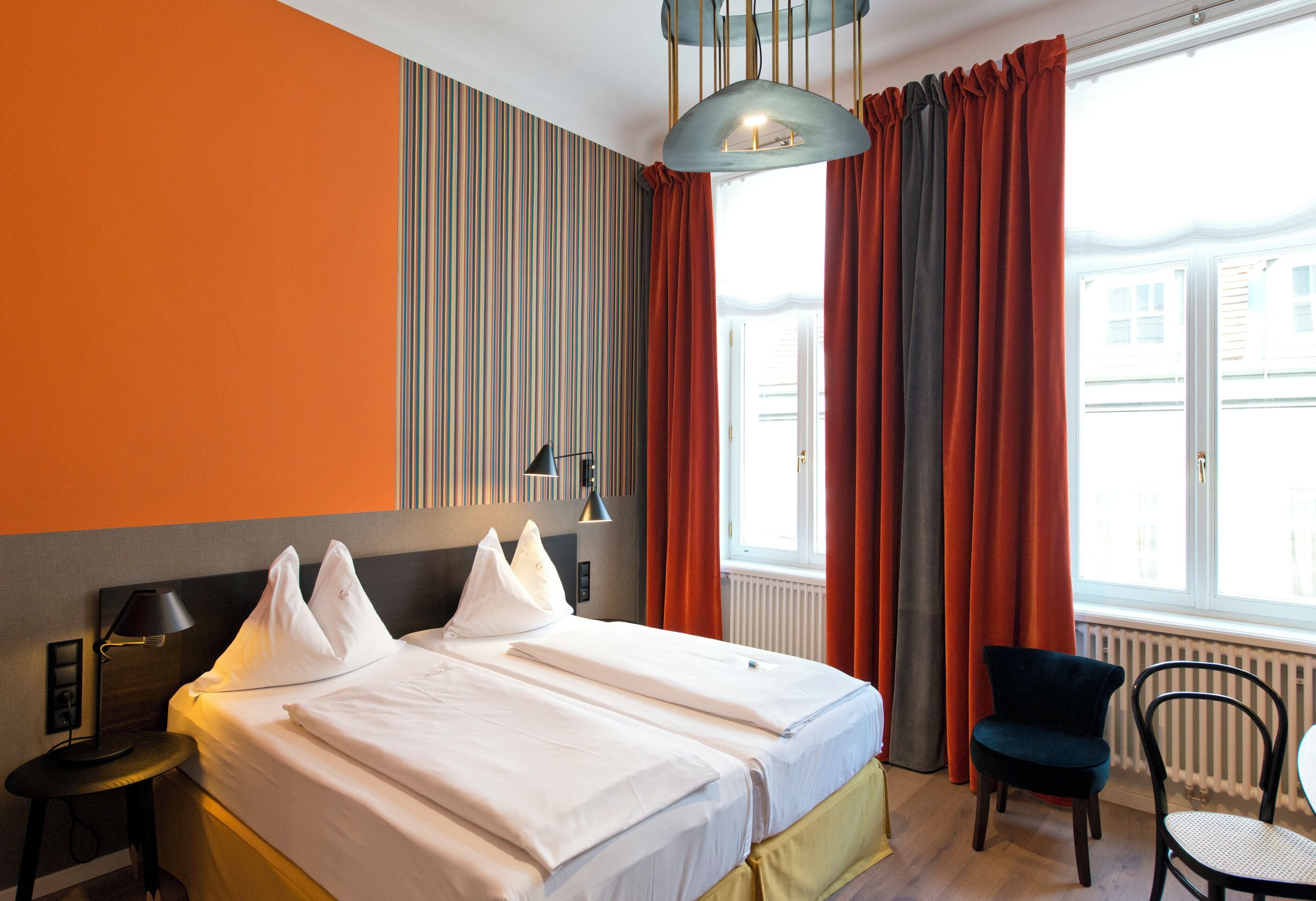 Une chambre d’hôtel avec un grand lit, deux tables de chevet, une chaise et une fenêtre avec des rideaux.