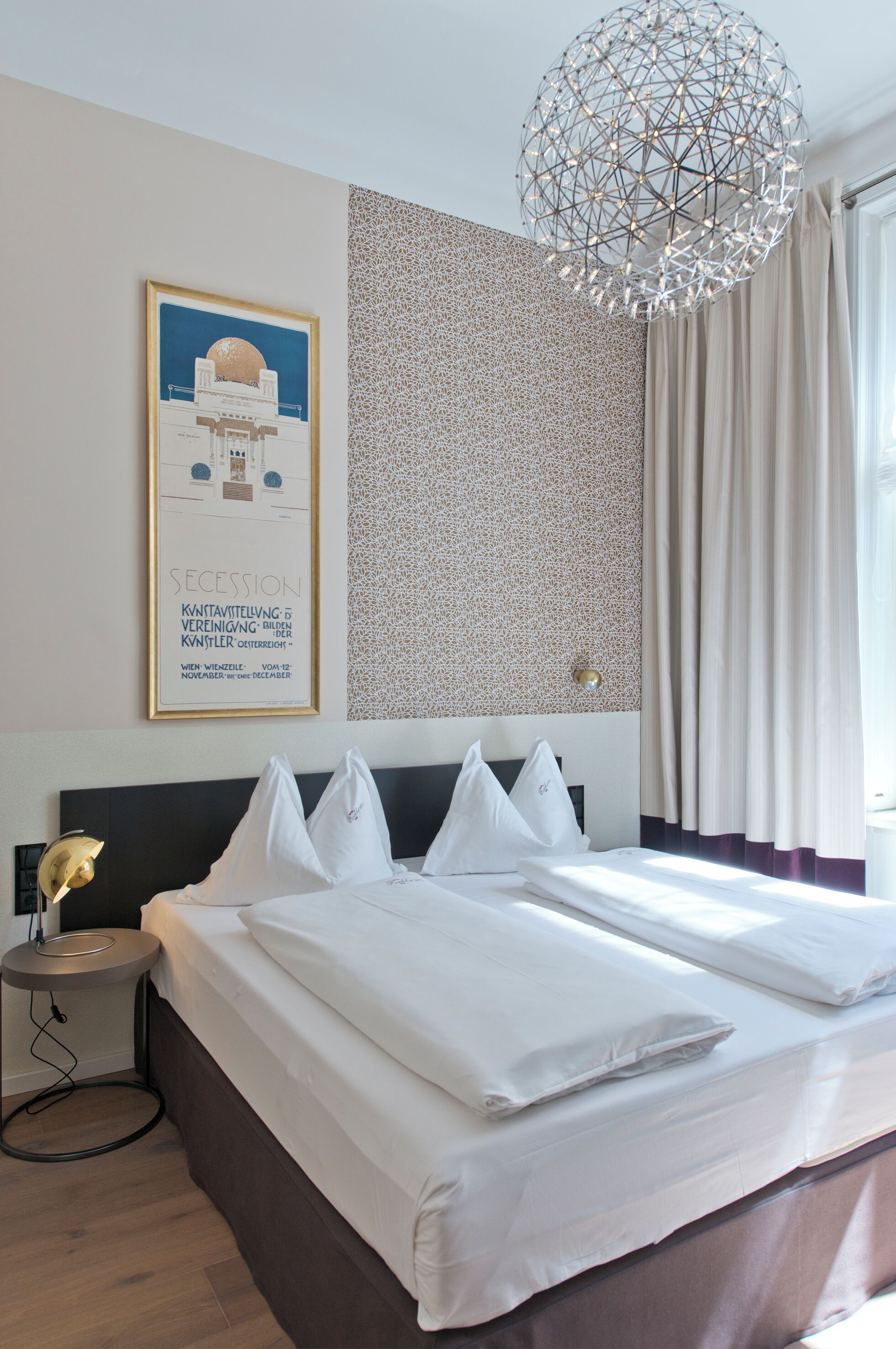 Quarto de hotel com cama bem arrumada, obra de arte na parede, papel de parede estampado e lustre moderno.