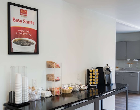 A kitchen area with a coffee station, including a coffee maker, cups, and coffee packets.