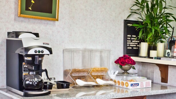 Un comptoir de cuisine avec une machine à café, un vase de fleurs et un tableau affichant le menu.