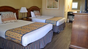 Une chambre d’hôtel avec deux lits, une commode en bois, un bureau avec un ordinateur et une salle de bain visible à travers une porte ouverte.