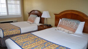 A hotel room with two beds, each with a patterned bedspread and pillows, a bedside table with a lamp, and a window with blinds. - Valley Inn San Jose (San Jose)