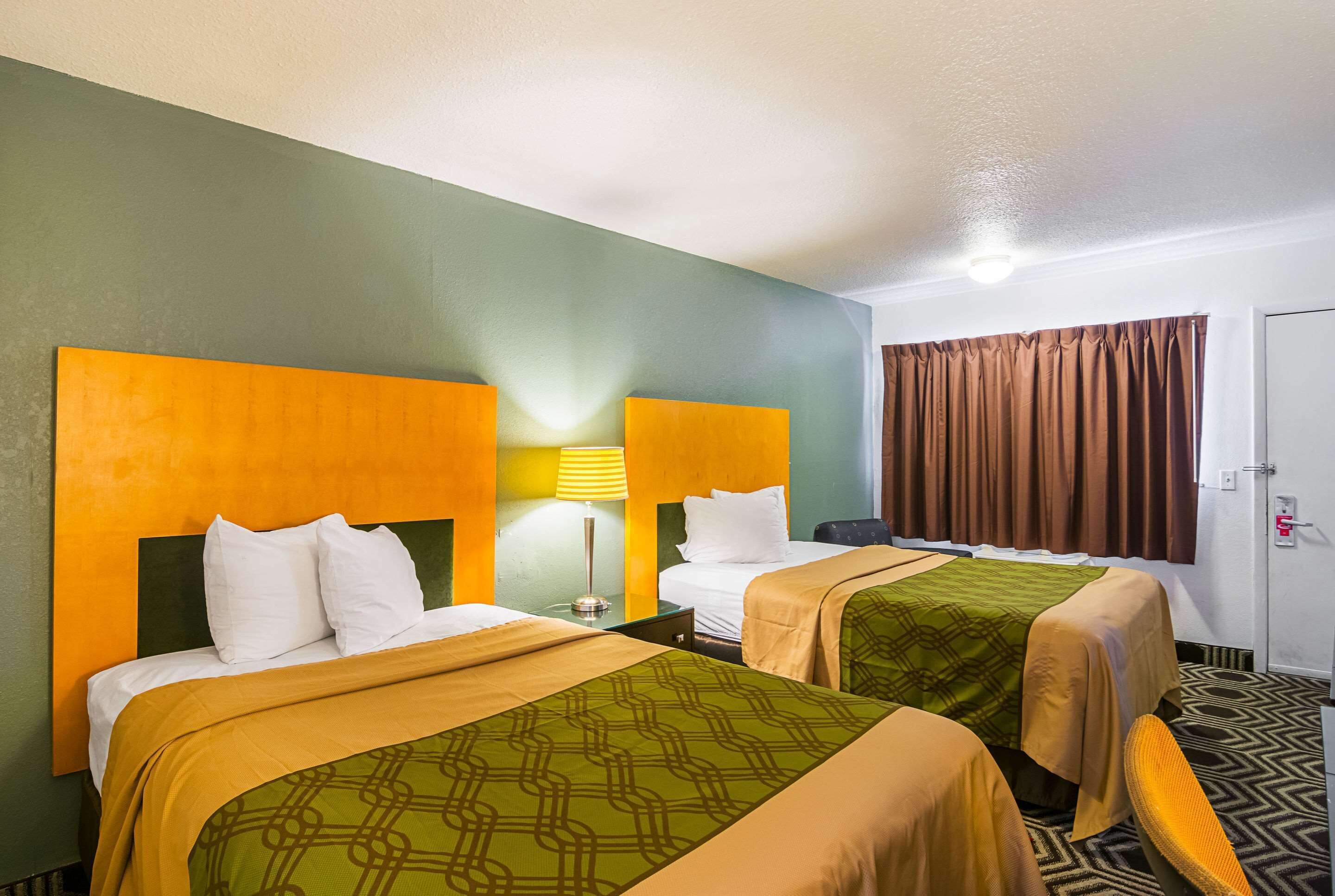 A hotel room with two beds, each with a headboard, a bedside lamp, and a window with curtains.