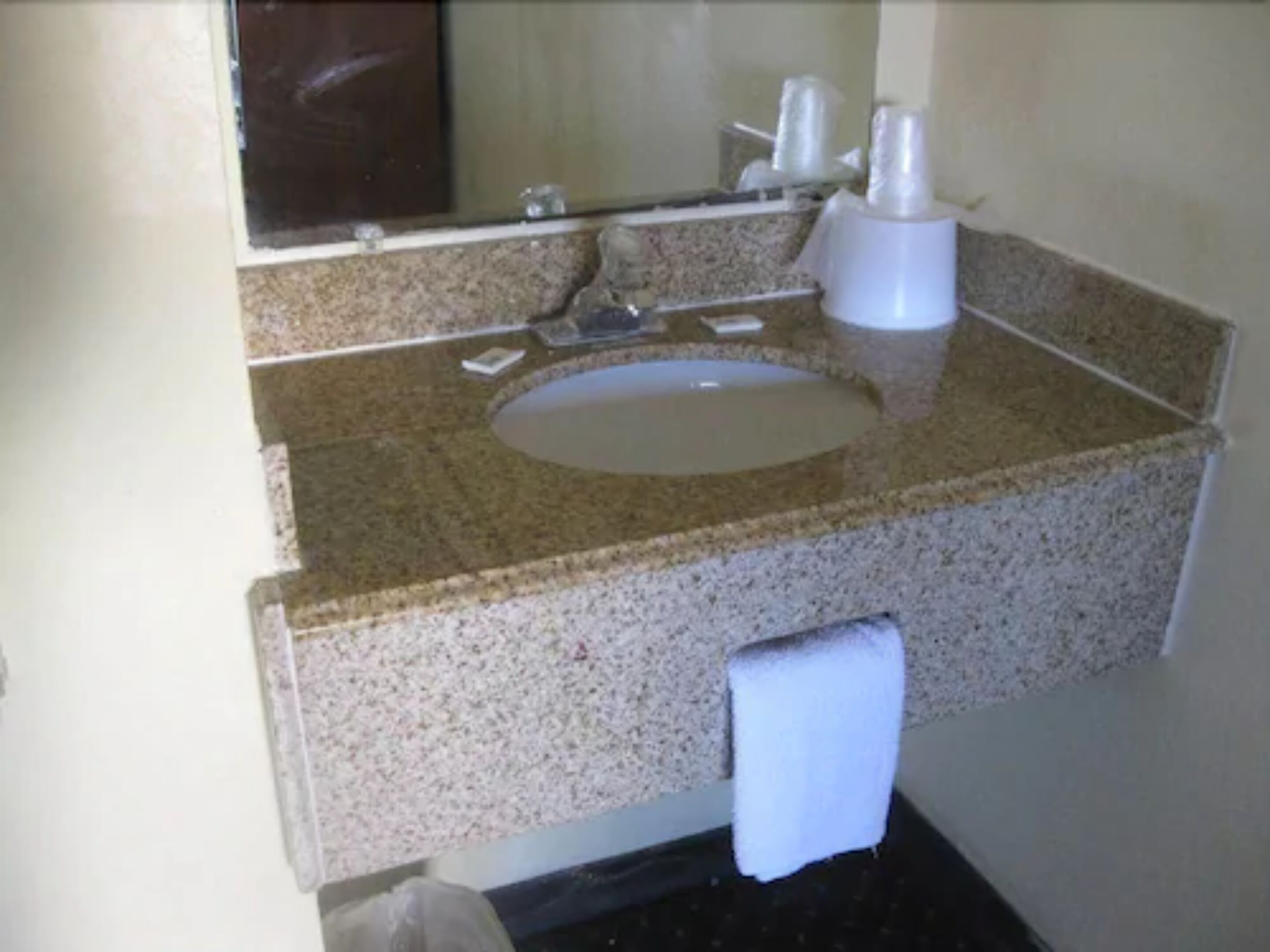 A bathroom with a granite countertop, a sink, a mirror, and a towel hanging on a rack.