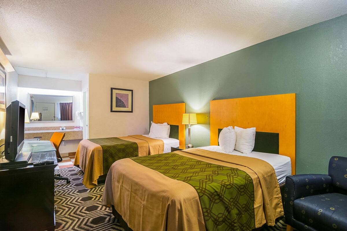 Een hotelkamer met twee bedden, een bureau met een computer en een stoel.