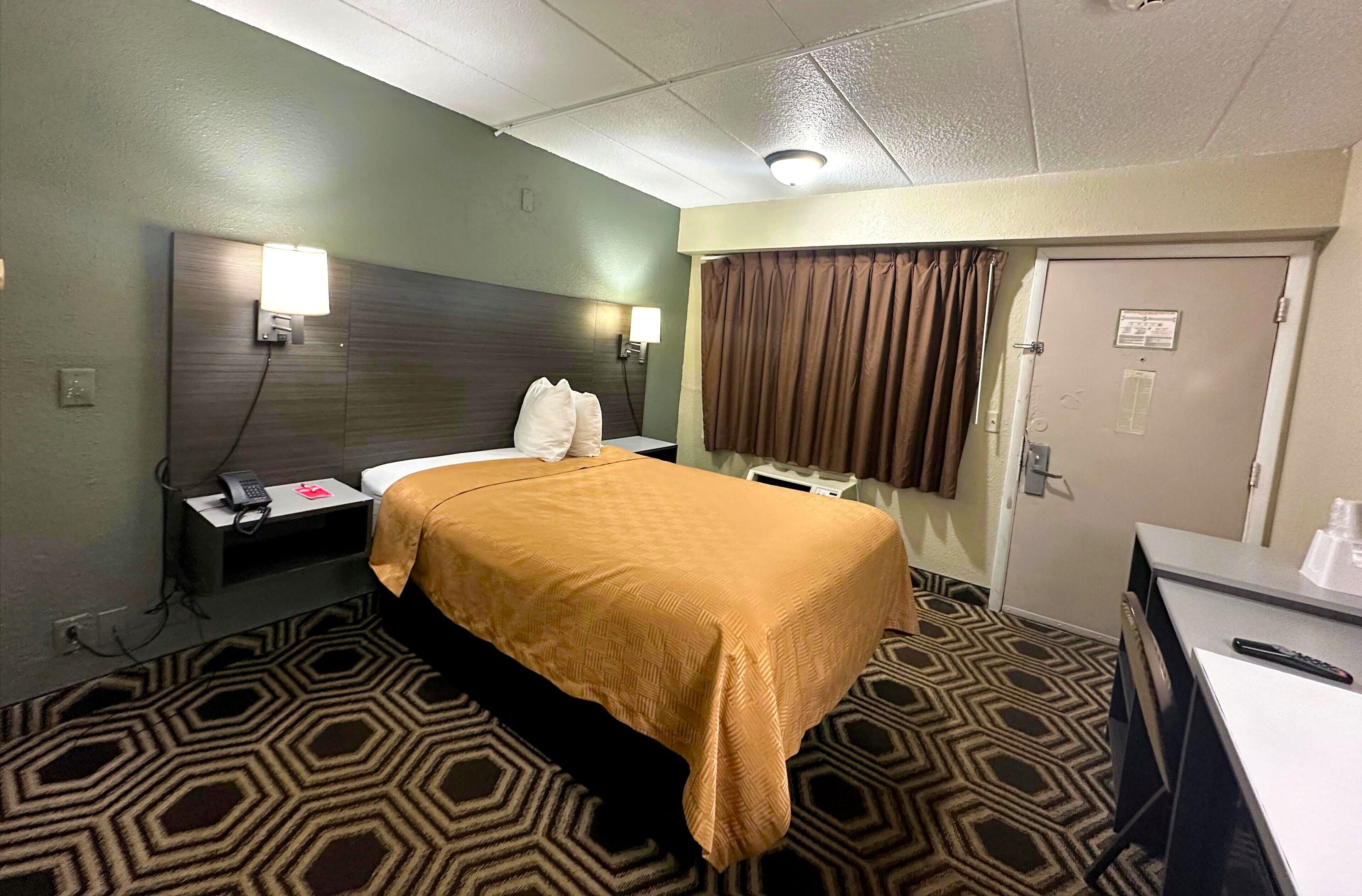 A hotel room with a bed, bedside table, lamp, and a desk with a chair.