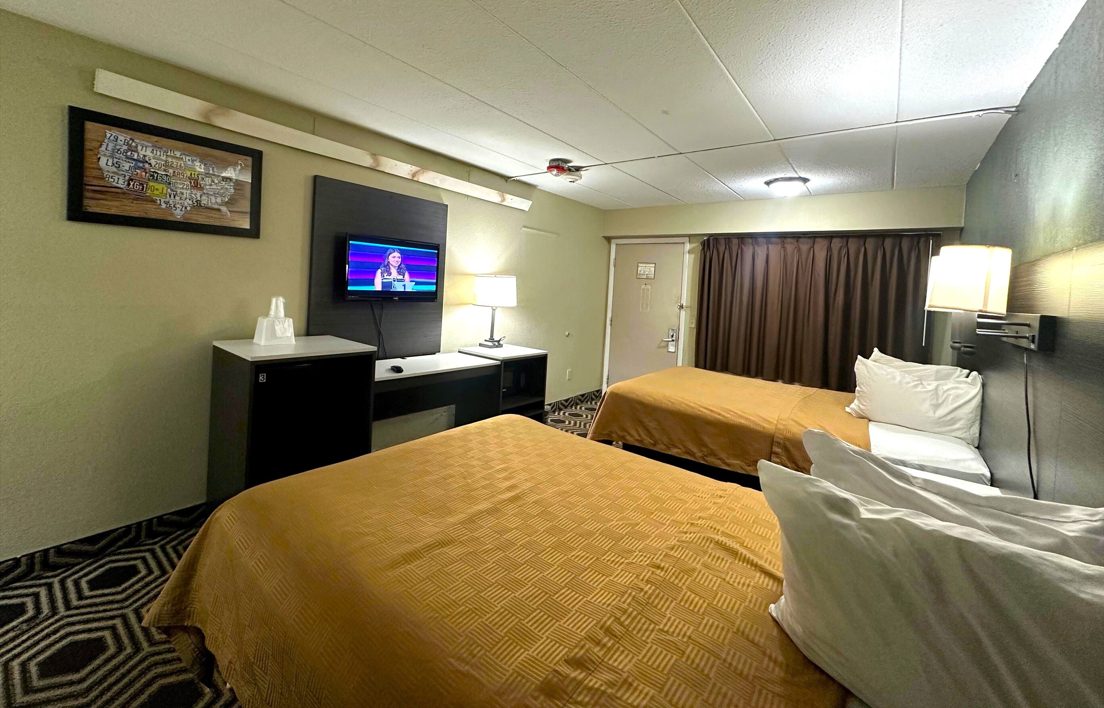 A hotel room with two beds, a desk, a television, and a door.