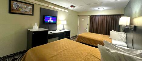 A hotel room with two beds, a desk, a television, and a door.