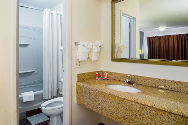 A bathroom with a white bathtub, a toilet, a sink with a granite countertop, and a mirror with a gold frame.
