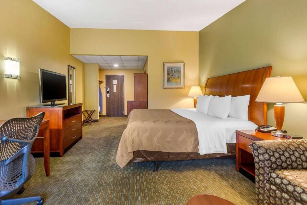 A hotel room with a bed, desk, chair, TV, and lamps.