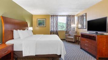 A hotel room with a bed, a TV, a chair, a desk, and a painting on the wall.