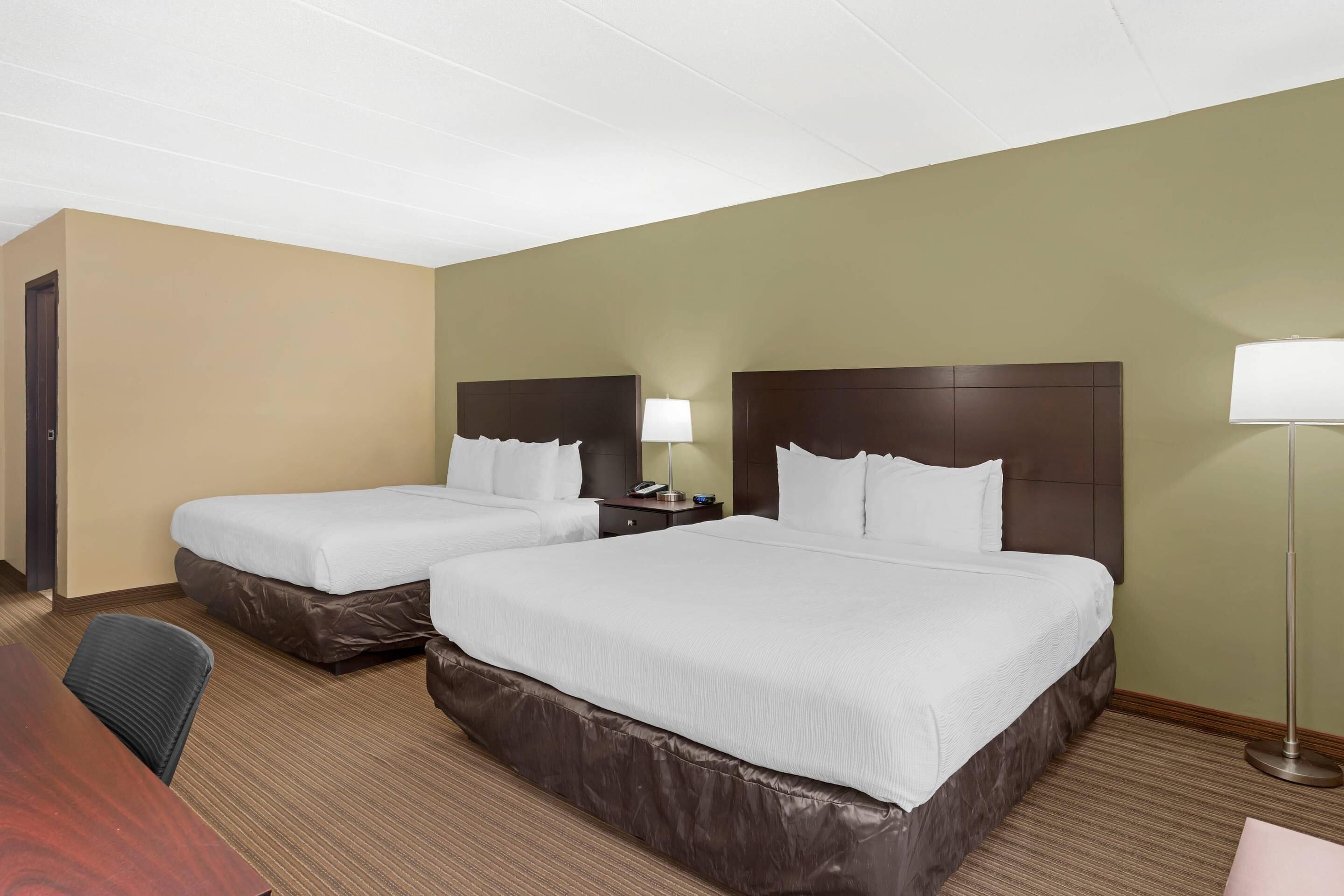 Une chambre d’hôtel avec deux lits, un bureau, une chaise, une lampe et une table de chevet.