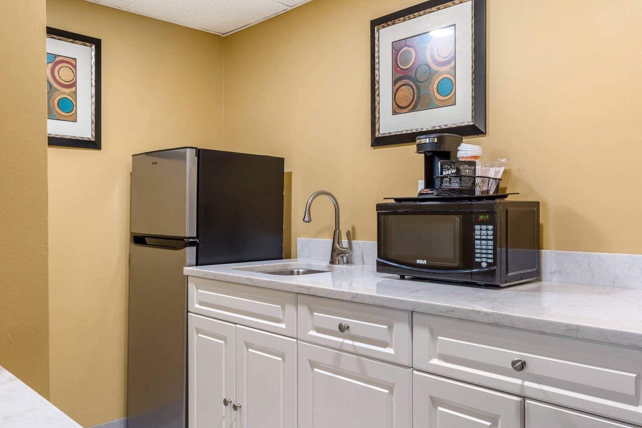 A kitchenette with a refrigerator, microwave, sink, and coffee maker.