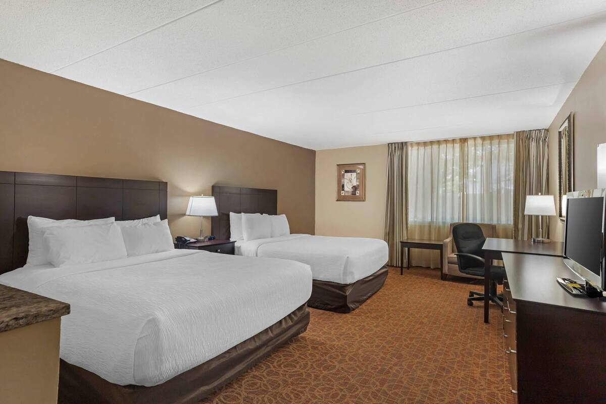 A hotel room with two beds, a desk, a chair, a TV, and a window with curtains.