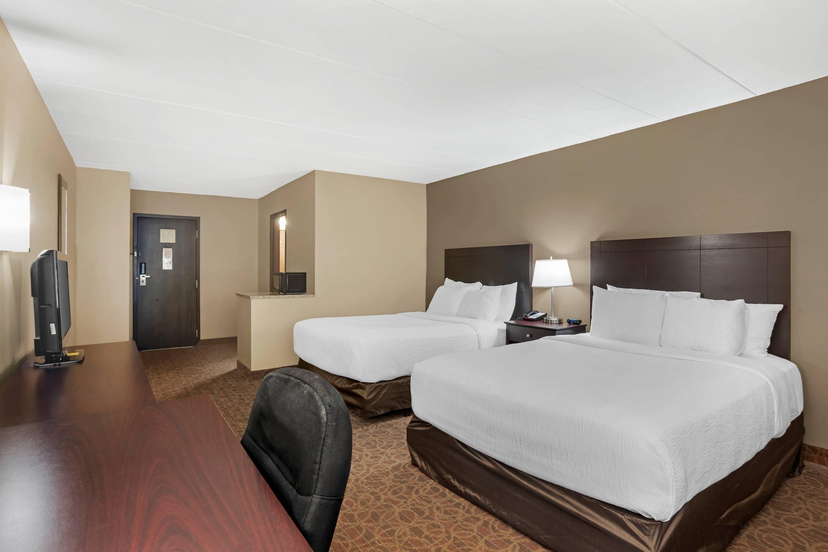 Une chambre d’hôtel avec deux lits, un bureau, une chaise, une télévision et une porte.