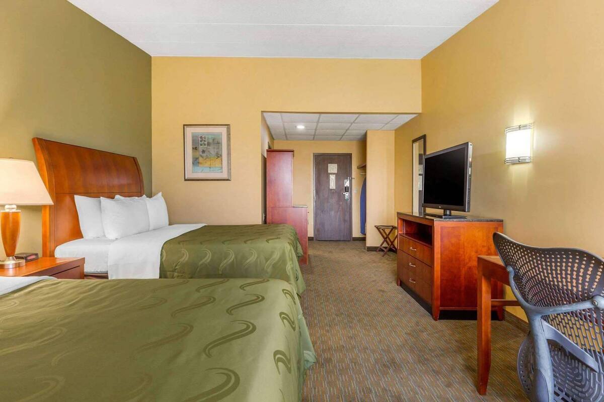 A hotel room with two beds, a TV, a desk, and a chair.