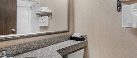 A bathroom with a granite countertop, a sink, a toilet, a mirror, and a towel rack.