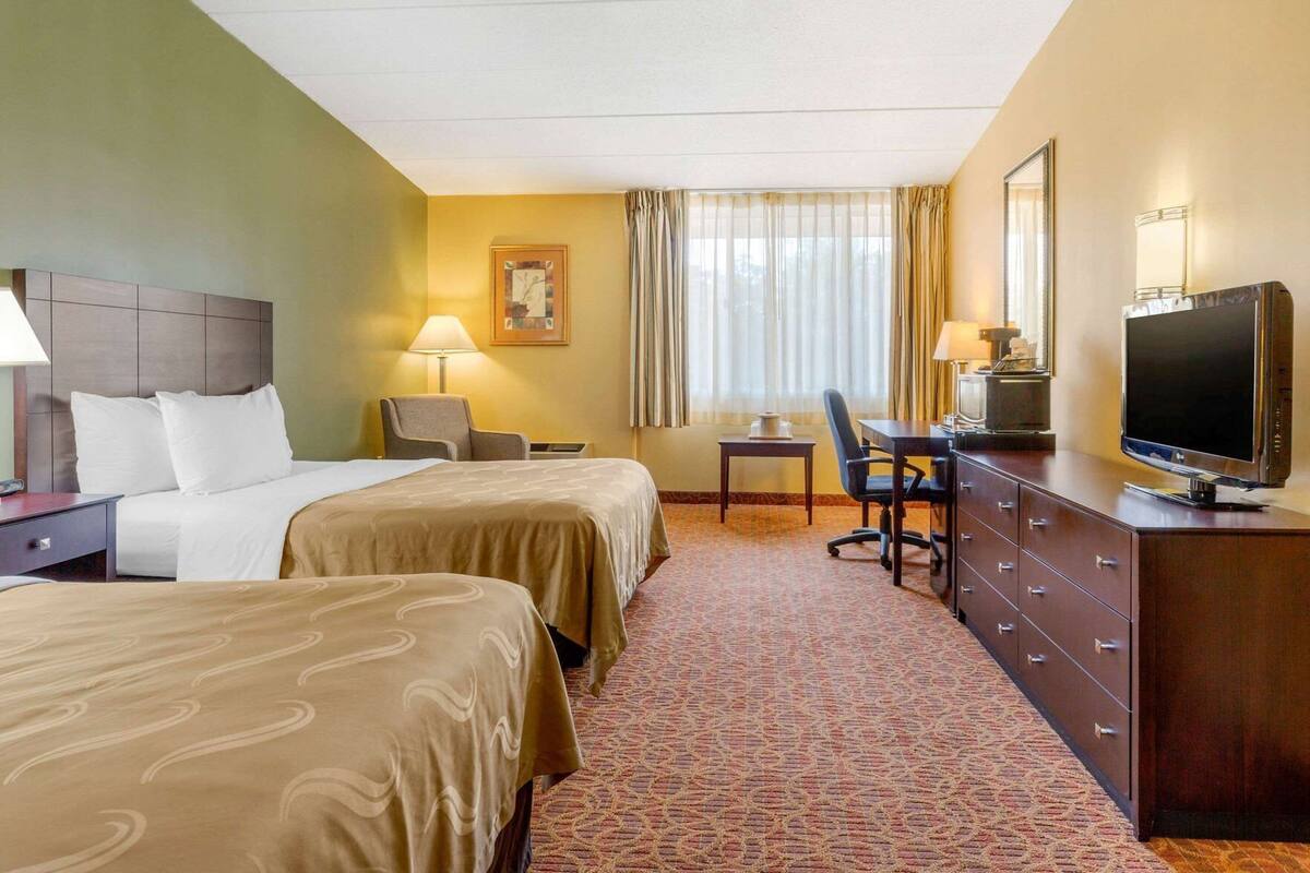 A hotel room with two beds, a desk, a television, and a chair.