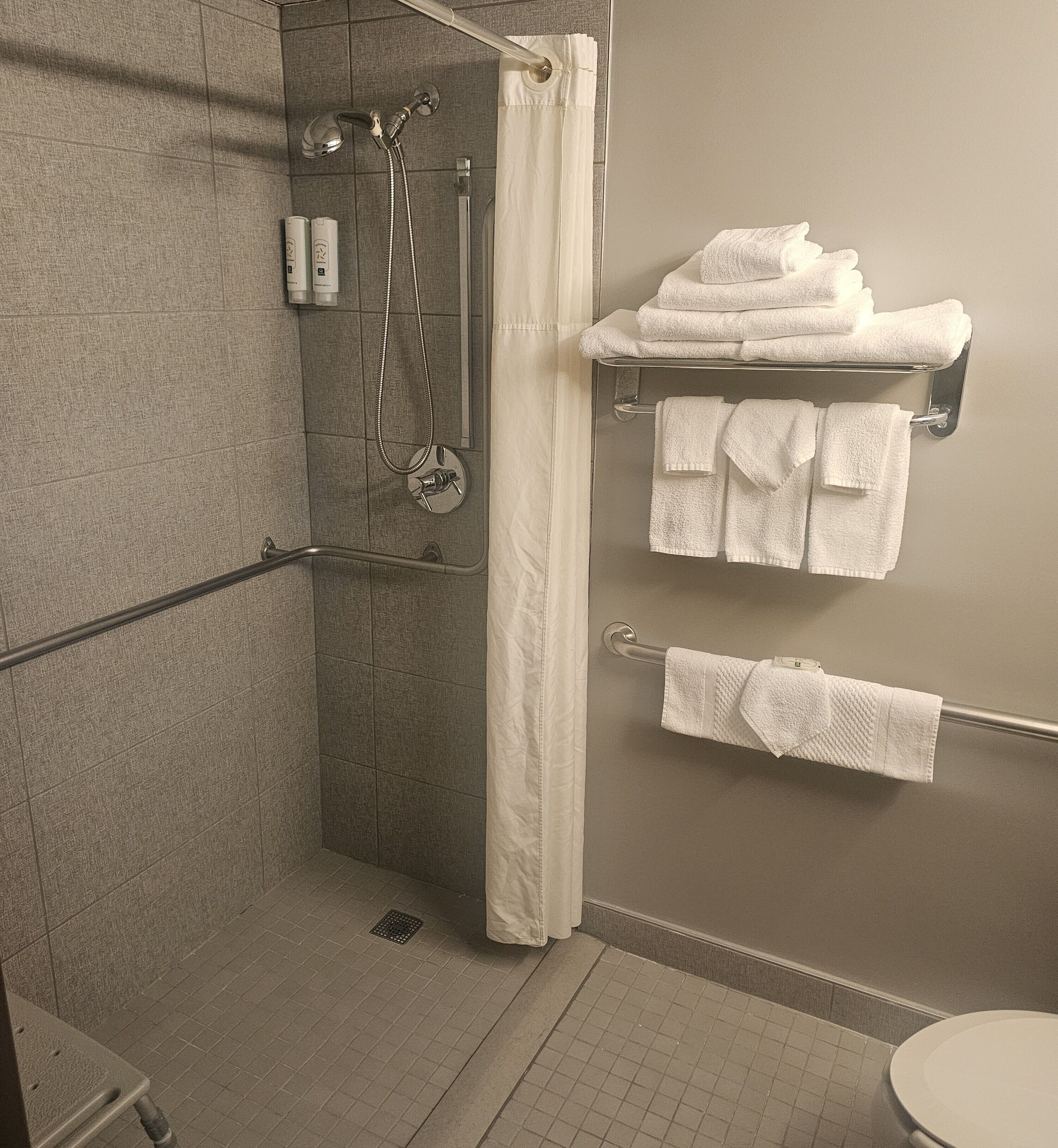 A bathroom with a shower, a toilet, and a towel rack with folded towels.