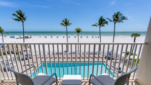 A balcony with a pool, white chairs, and a view of the beach and ocean. - Best Western Plus Beach Resort (Fort Myers Beach)