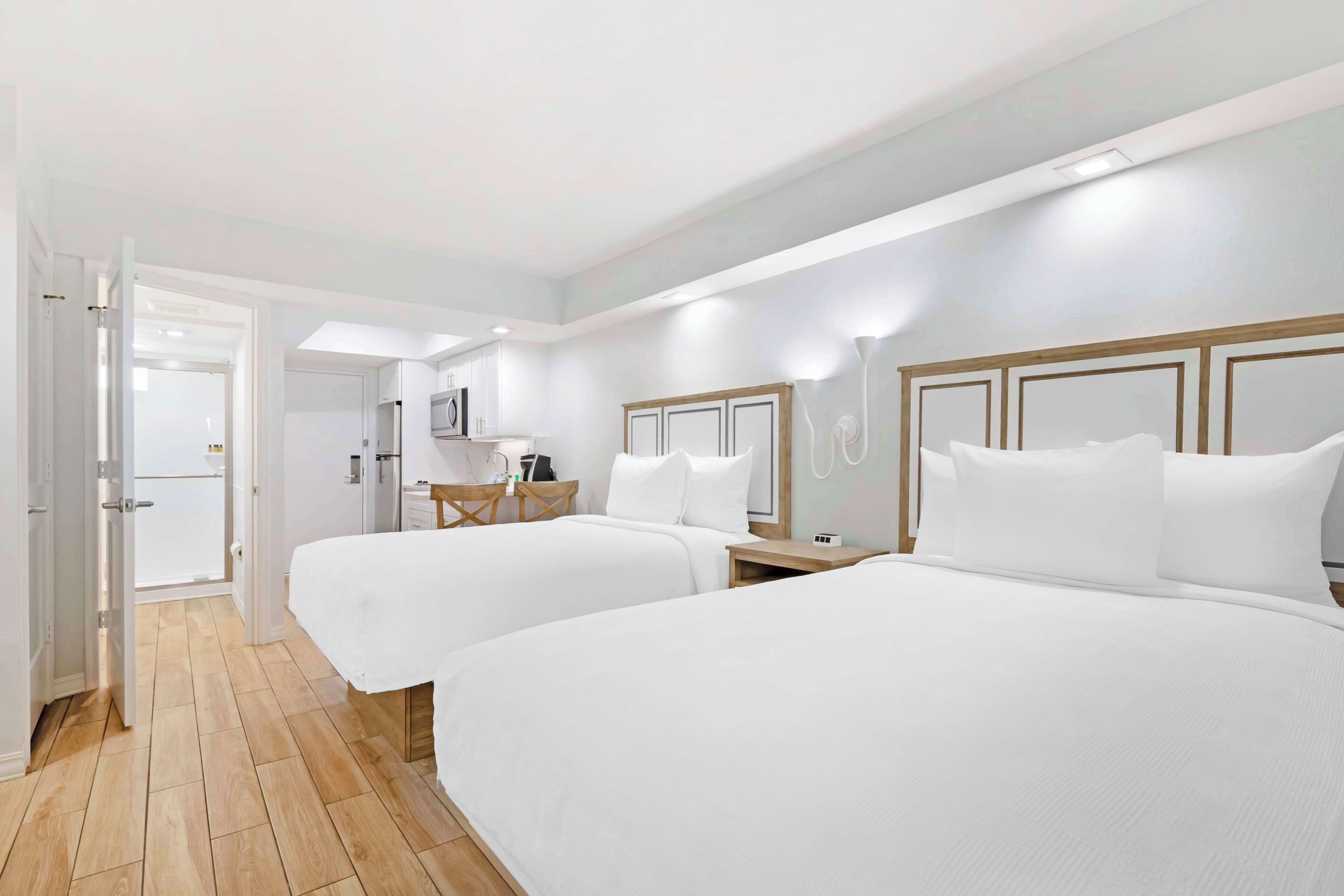 A hotel room with two beds, a desk, and a chair. There is a door leading to another room and a bathroom.