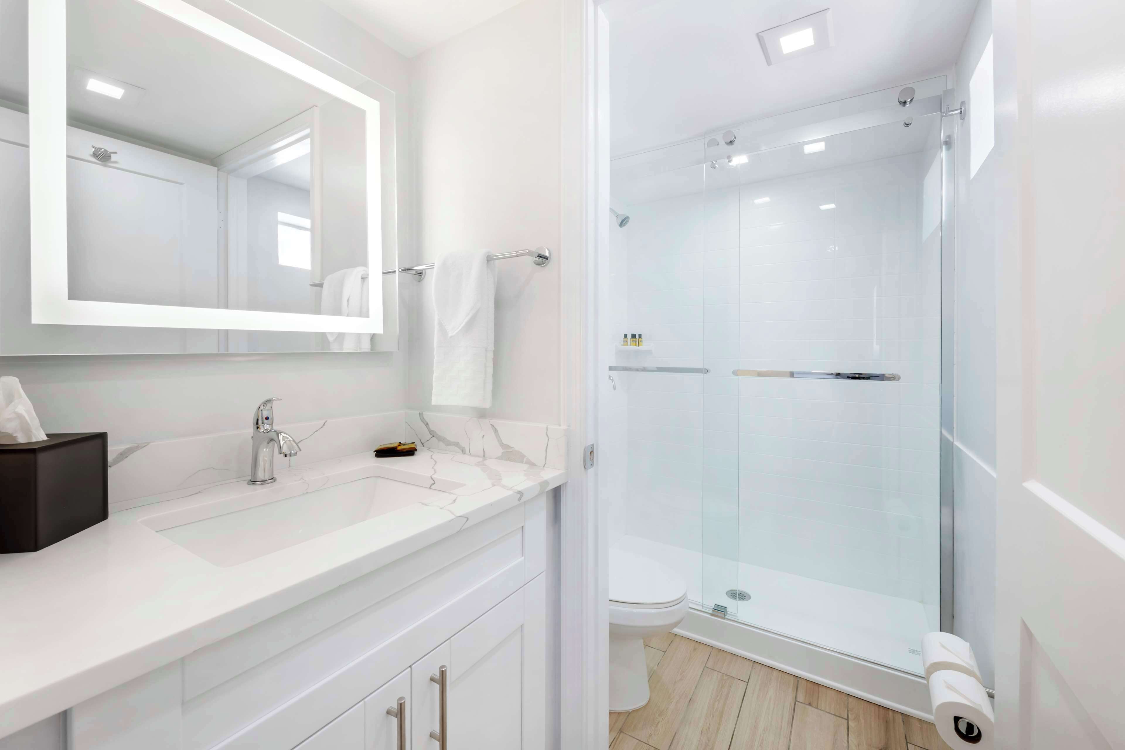A modern bathroom with a large mirror, white vanity, and a glass-enclosed shower.