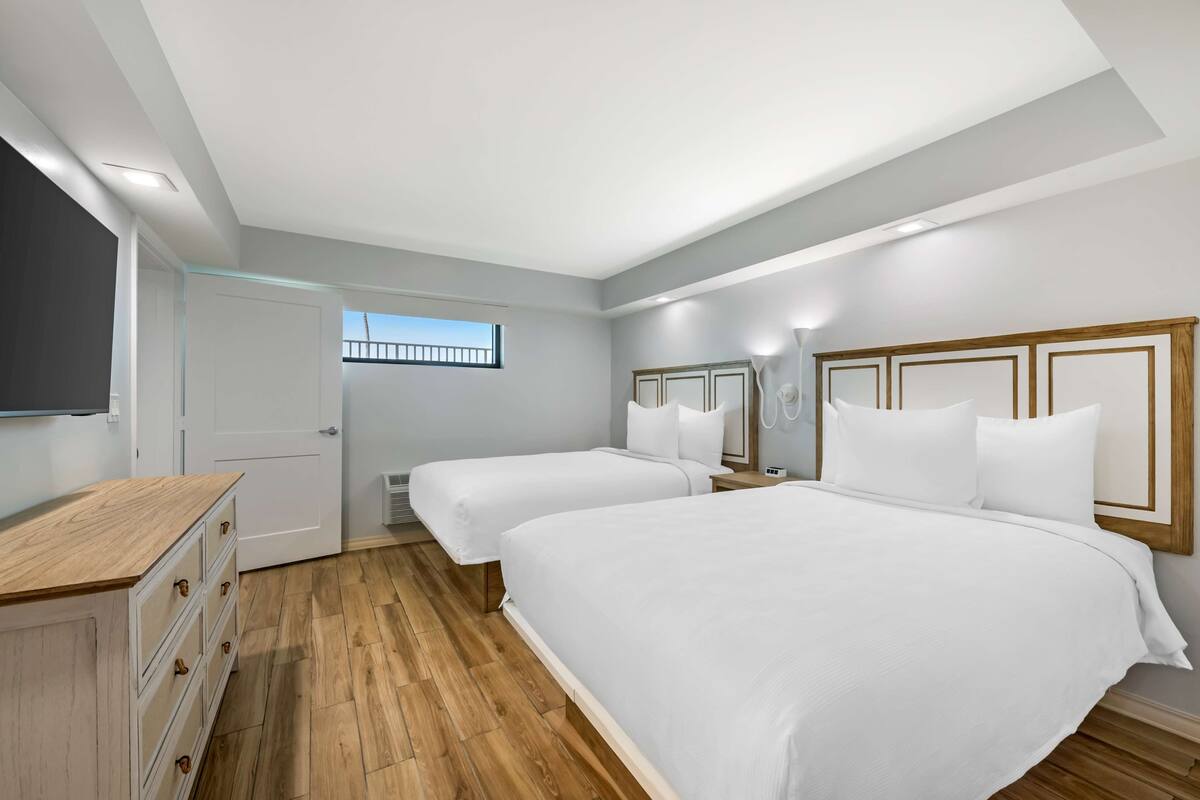 Habitación de hotel con dos camas, un aparador de madera, un televisor de pantalla plana y ventana con vista al balcón.