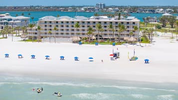 A beachfront hotel with multiple balconies, a pool area, and beach umbrellas.