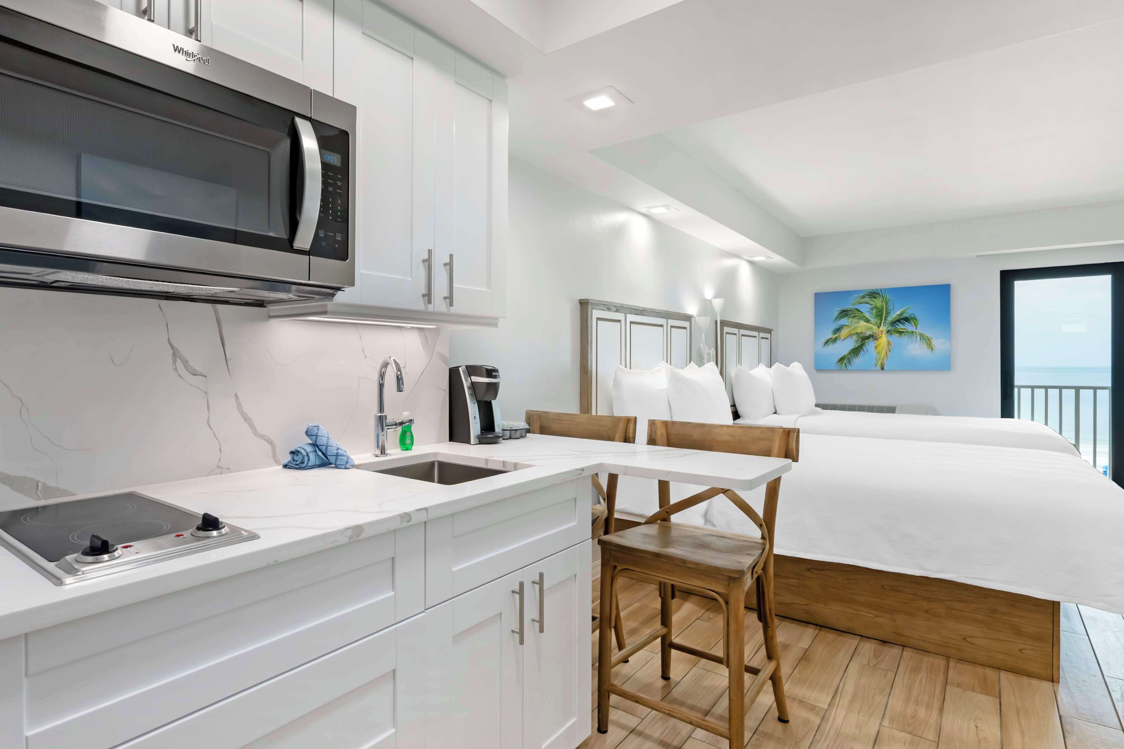 A modern hotel room with a kitchenette, a bed, a dining area, and a large window with a view.