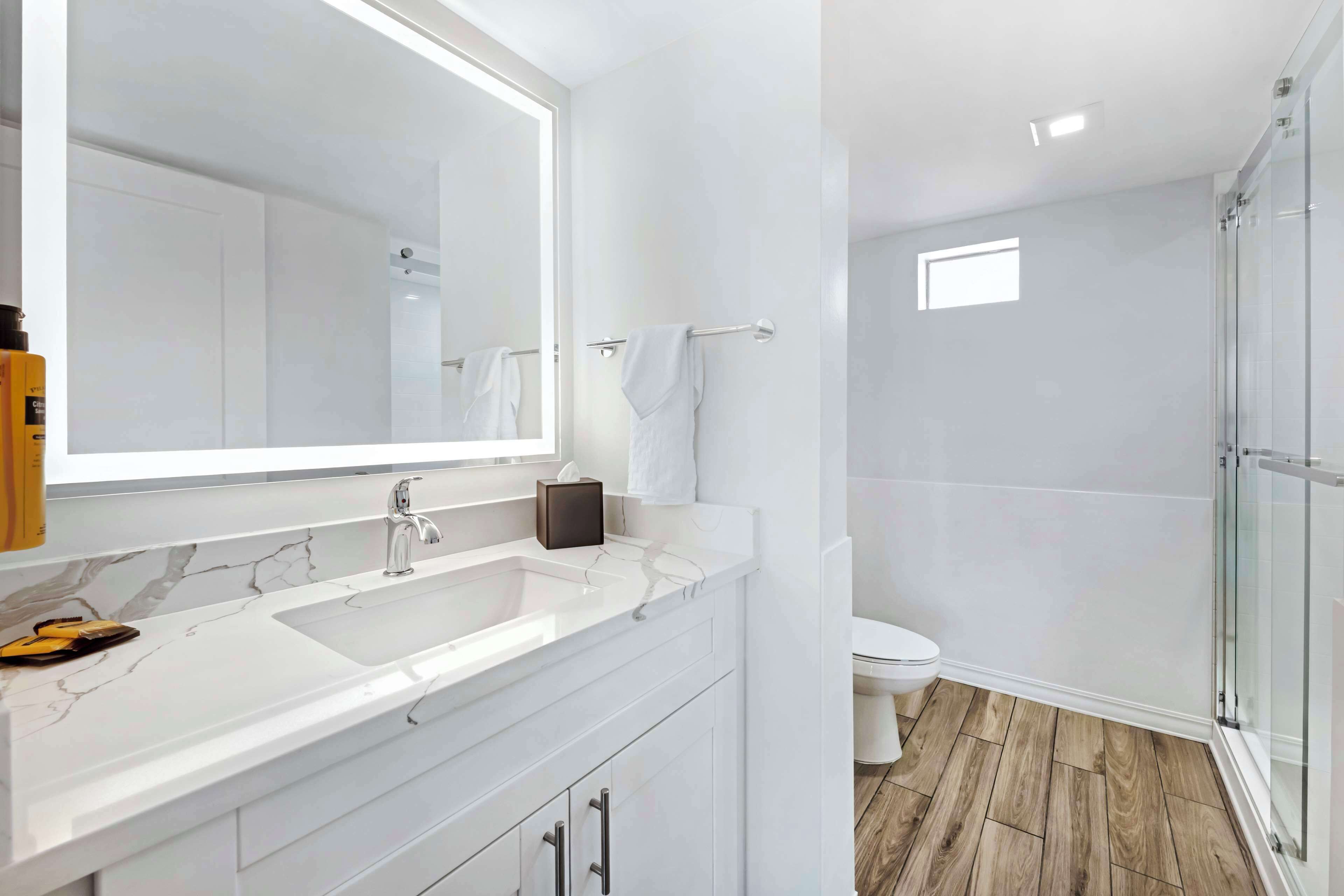A modern bathroom with a large mirror, white vanity, and a glass shower enclosure.