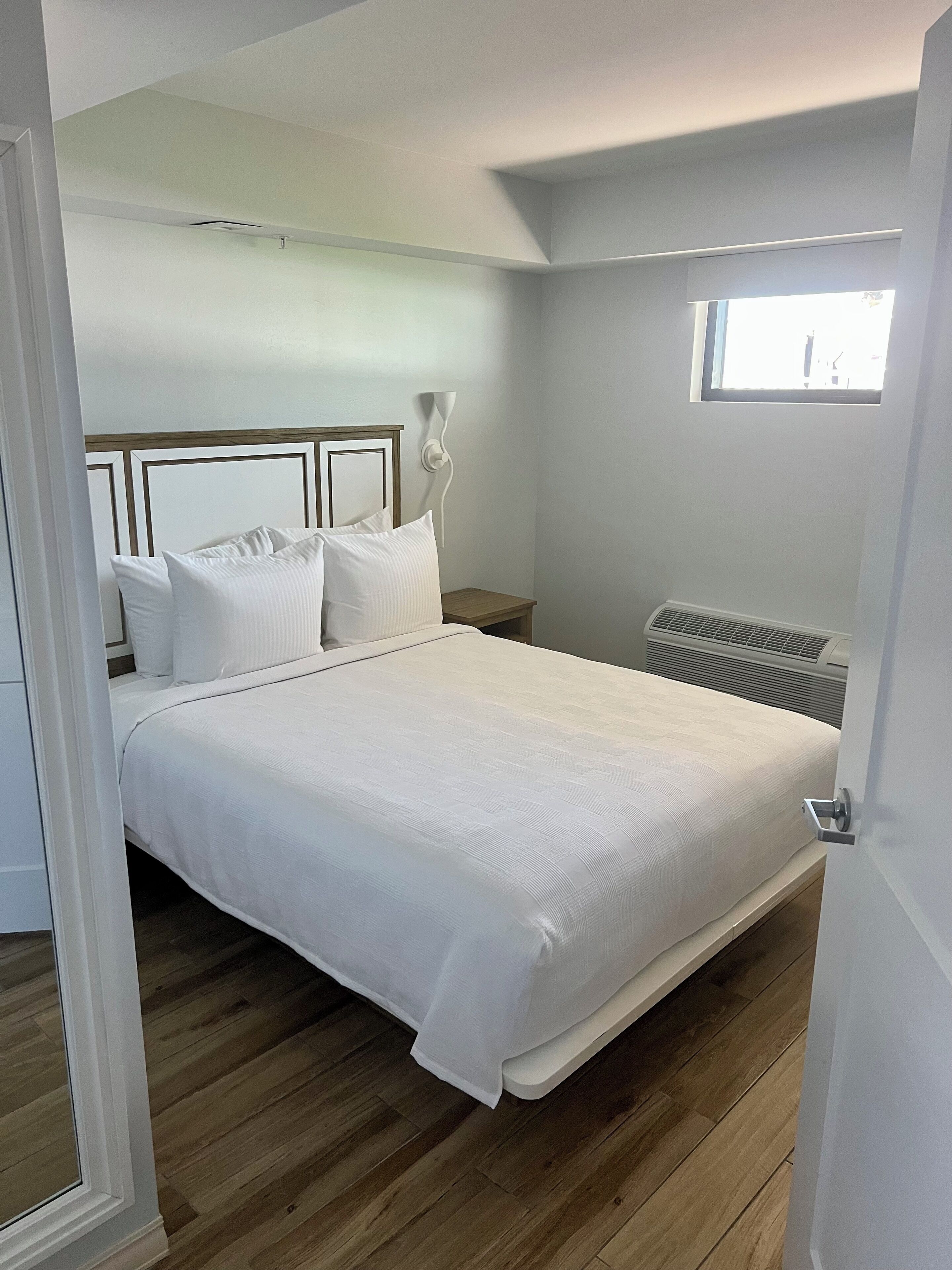 A bedroom with a large bed, a bedside table, a wall-mounted light, and a window.